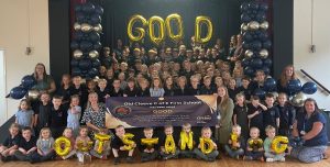 Group photo of children and staff with a banner, sat with balloons spelling out "GOOD" and "OUTSTANDING"